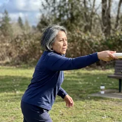 Cris M. mid-throw outdoors with her right arm in full follow-through after throwing a frisbee