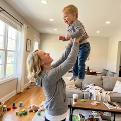 Megan lifting her toddler with both arms overhead at home